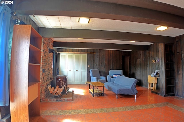 sitting room featuring wooden walls, beam ceiling, and a wood stove