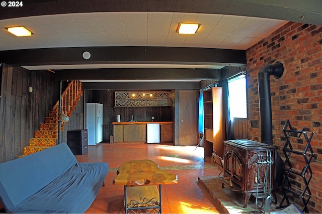 living room with a wood stove, beam ceiling, brick wall, and wood walls