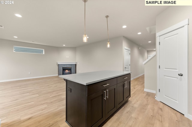 kitchen featuring light wood-type flooring, dark brown cabinetry, pendant lighting, a fireplace, and a center island