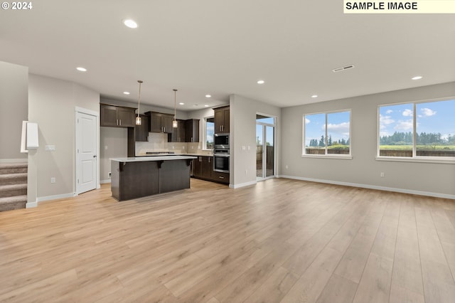 kitchen featuring a center island, hanging light fixtures, backsplash, dark brown cabinets, and light wood-type flooring