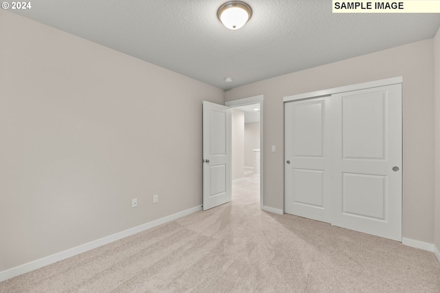 unfurnished bedroom with a textured ceiling, light colored carpet, and a closet