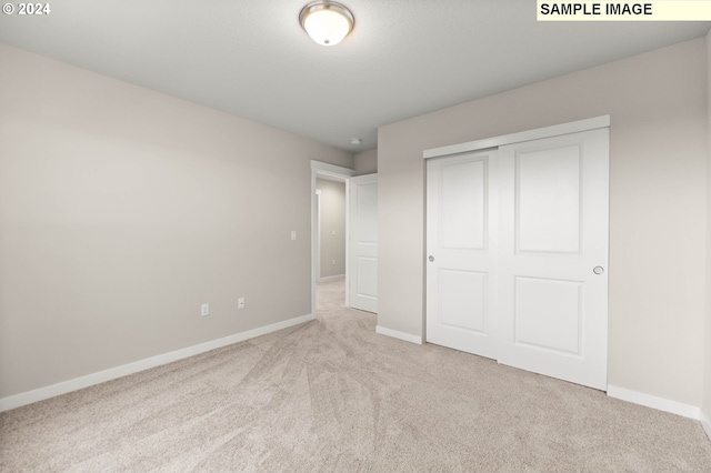 unfurnished bedroom with light colored carpet and a closet