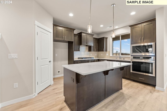 kitchen with a breakfast bar, a center island, hanging light fixtures, appliances with stainless steel finishes, and light hardwood / wood-style floors