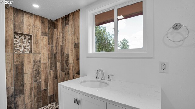 bathroom with a textured ceiling, tiled shower, and vanity