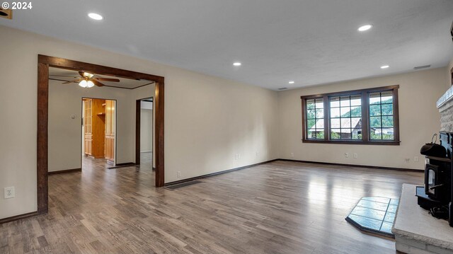 unfurnished living room with a wood stove, ceiling fan, and hardwood / wood-style floors