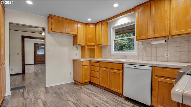 kitchen with light wood-type flooring, sink, decorative backsplash, tile countertops, and white dishwasher