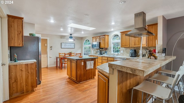 kitchen featuring a skylight, a center island, stainless steel appliances, kitchen peninsula, and island range hood