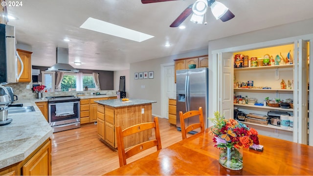 kitchen featuring appliances with stainless steel finishes, light wood-type flooring, a skylight, a center island, and range hood