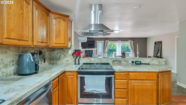 kitchen with stainless steel appliances, wall chimney range hood, tasteful backsplash, kitchen peninsula, and hardwood / wood-style floors