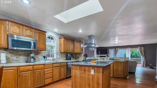 kitchen with wall chimney range hood, a kitchen island, a wealth of natural light, light hardwood / wood-style floors, and stainless steel appliances