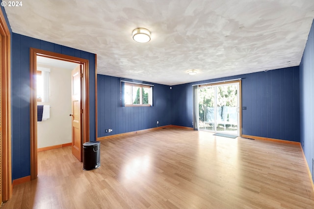 empty room featuring wooden walls, a textured ceiling, and light hardwood / wood-style floors