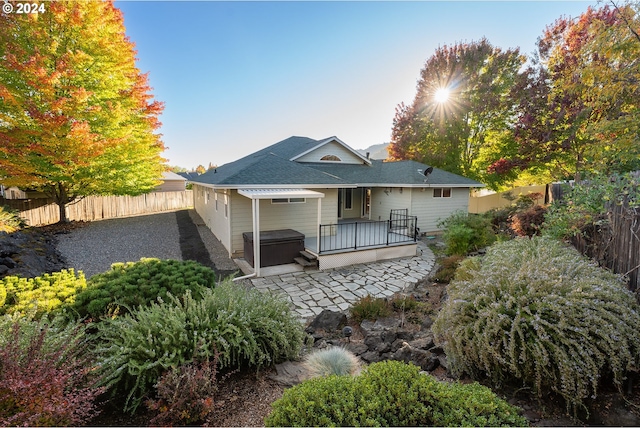 back of house with a fenced backyard, a hot tub, a patio area, and a shingled roof