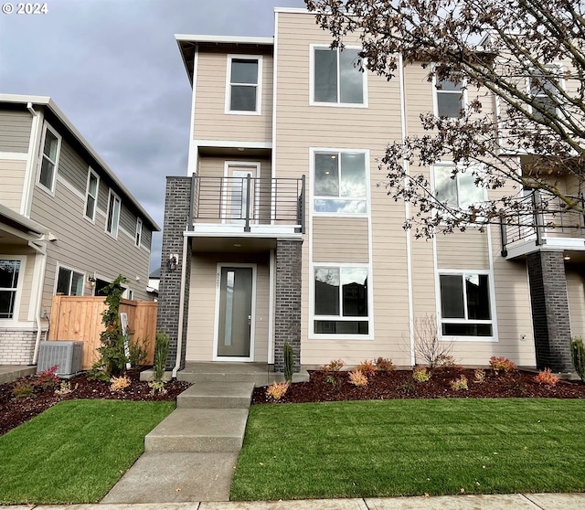 view of front of home with a balcony, central air condition unit, and a front lawn