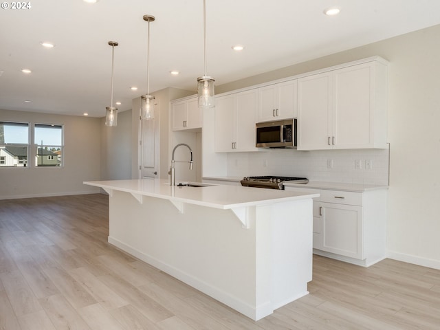 kitchen featuring decorative light fixtures, sink, stainless steel appliances, and a kitchen island with sink