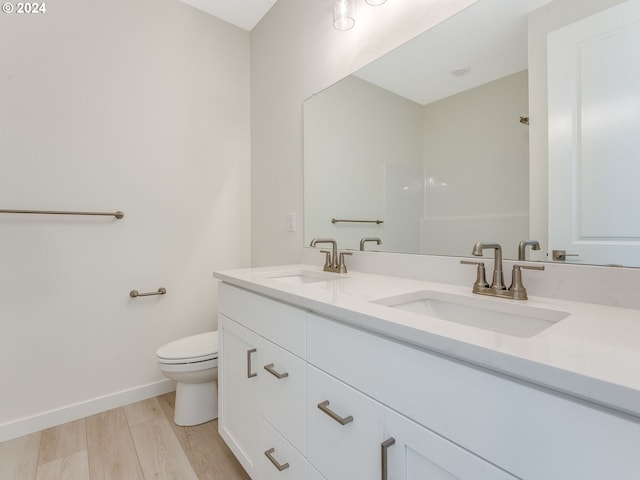 full bath with double vanity, toilet, a sink, and wood finished floors