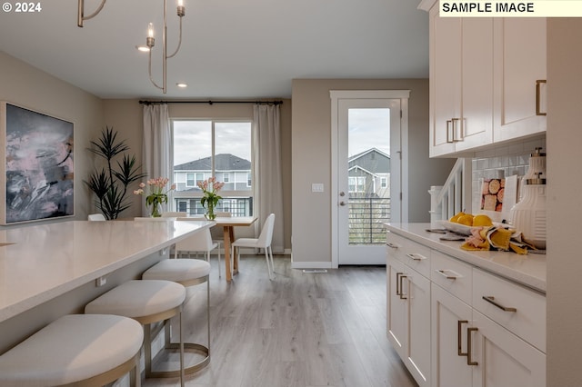 kitchen featuring pendant lighting, light wood-type flooring, tasteful backsplash, a notable chandelier, and white cabinetry