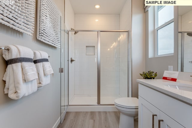 bathroom with hardwood / wood-style floors, vanity, toilet, and a shower with shower door