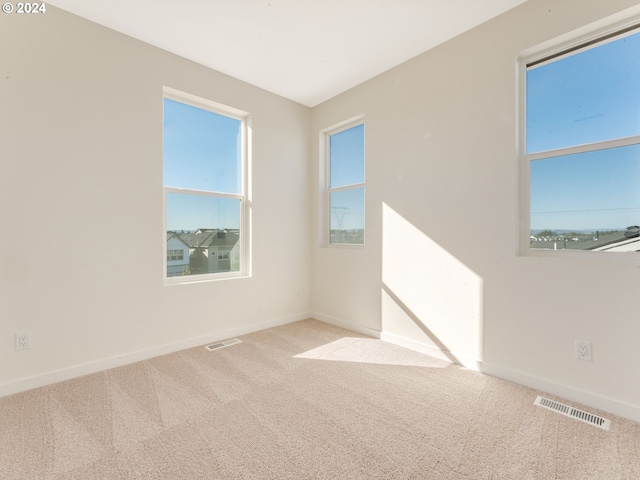 empty room with carpet flooring, baseboards, visible vents, and a wealth of natural light