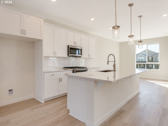 kitchen with a kitchen island with sink, light hardwood / wood-style flooring, stainless steel appliances, and decorative light fixtures