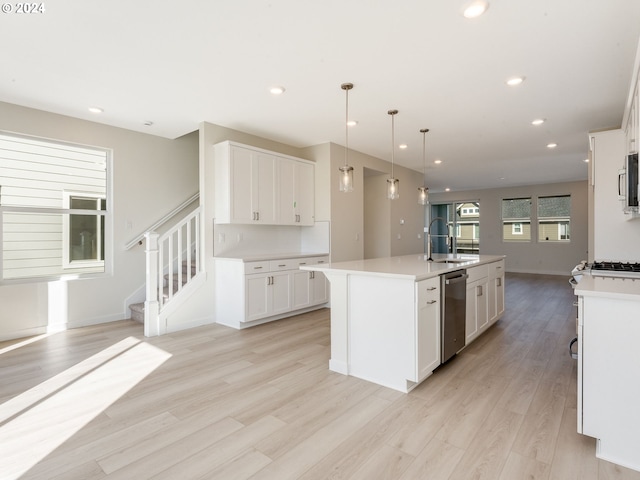 kitchen with a kitchen island with sink, sink, light hardwood / wood-style flooring, white cabinetry, and hanging light fixtures