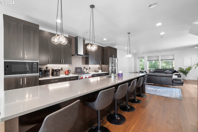 kitchen with a breakfast bar, light hardwood / wood-style flooring, wall chimney exhaust hood, decorative backsplash, and built in microwave