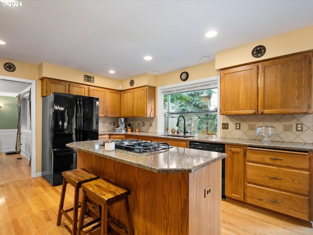 kitchen featuring light stone countertops, black appliances, sink, a kitchen island, and light hardwood / wood-style floors