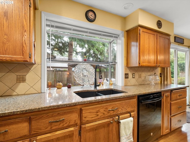 kitchen with black dishwasher, sink, light stone counters, light hardwood / wood-style floors, and tasteful backsplash