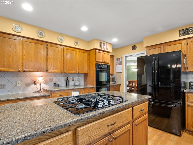 kitchen featuring light hardwood / wood-style floors, black appliances, dark stone counters, and backsplash