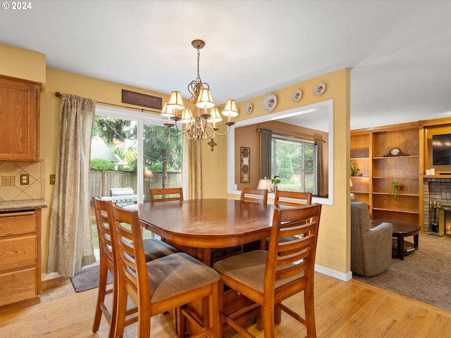 dining room with a notable chandelier, light wood-type flooring, and a brick fireplace