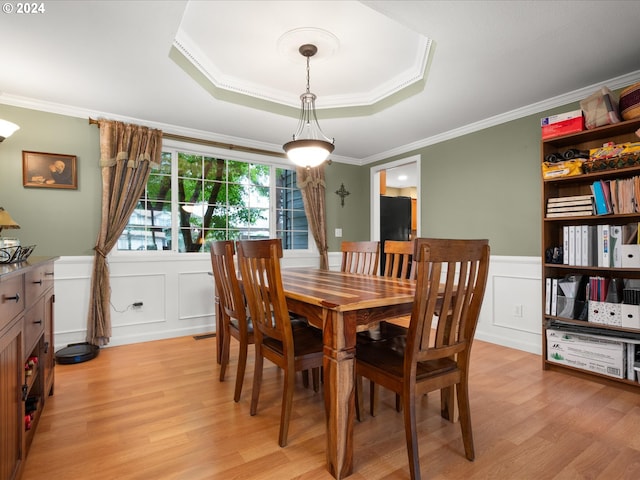 dining room with light hardwood / wood-style flooring, ornamental molding, and a raised ceiling