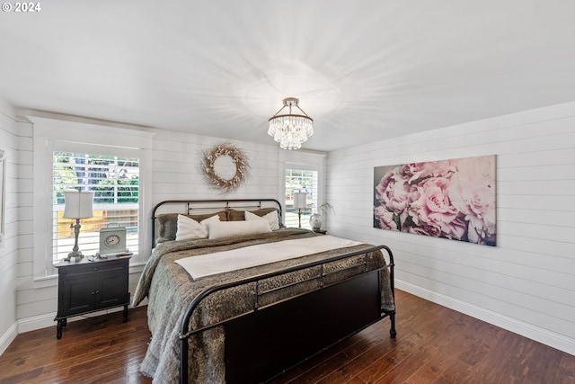 bedroom with dark wood-type flooring, wood walls, and an inviting chandelier