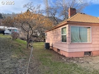 view of side of home with central AC, a yard, and a chimney