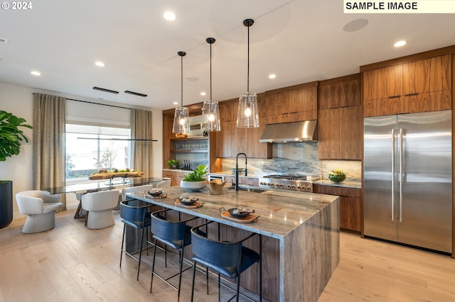 kitchen featuring sink, tasteful backsplash, an island with sink, stainless steel appliances, and exhaust hood