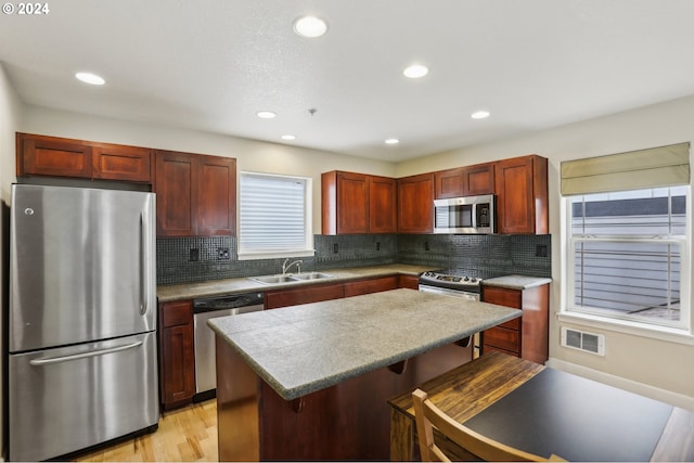 kitchen featuring sink, a center island, stainless steel appliances, light hardwood / wood-style floors, and a breakfast bar