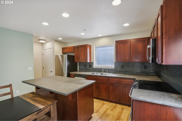 kitchen with a kitchen breakfast bar, sink, light wood-type flooring, appliances with stainless steel finishes, and tasteful backsplash