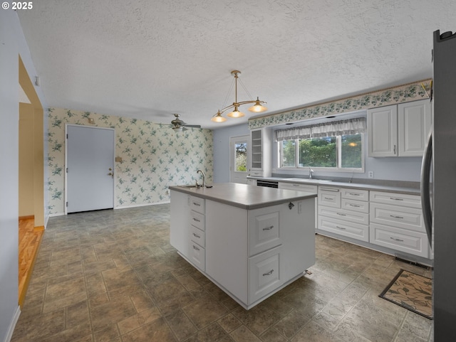 kitchen featuring wallpapered walls, a sink, white cabinetry, a textured ceiling, and freestanding refrigerator
