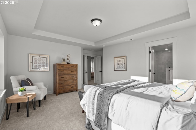 bedroom with light carpet, ensuite bathroom, and a raised ceiling