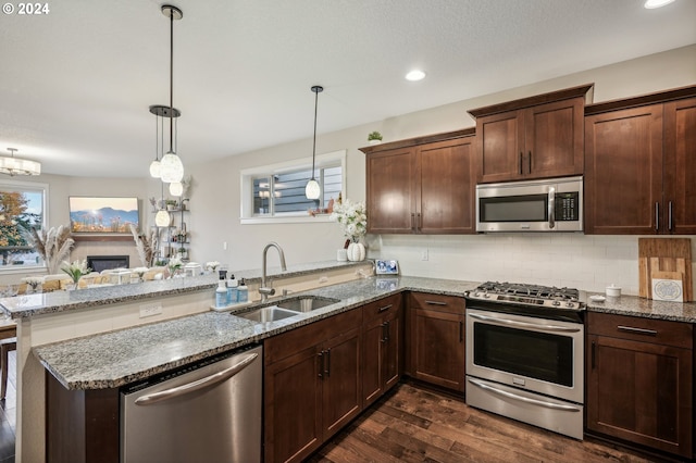 kitchen featuring light stone countertops, sink, dark wood-type flooring, hanging light fixtures, and appliances with stainless steel finishes