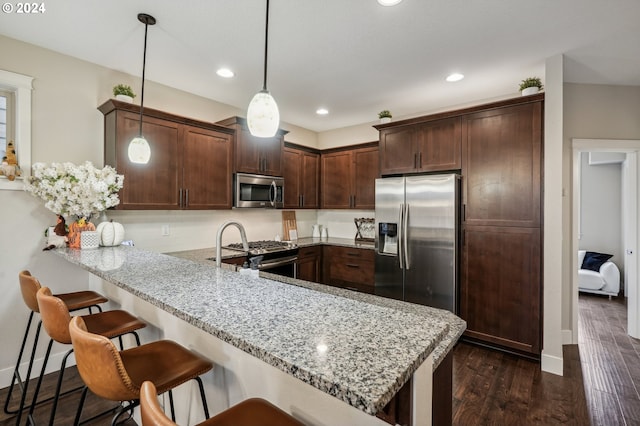 kitchen featuring pendant lighting, dark wood-type flooring, appliances with stainless steel finishes, light stone counters, and kitchen peninsula