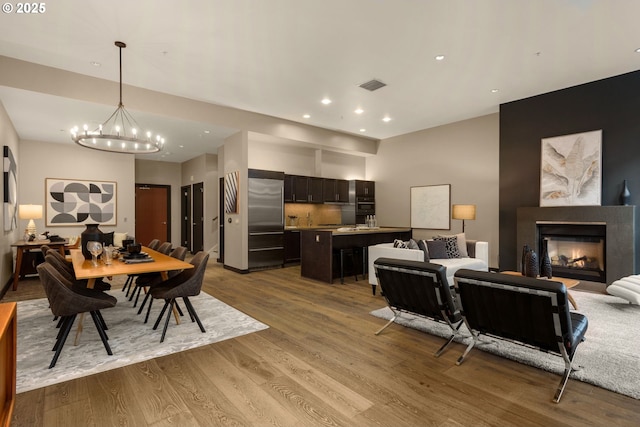 dining space with recessed lighting, wood finished floors, visible vents, a glass covered fireplace, and an inviting chandelier