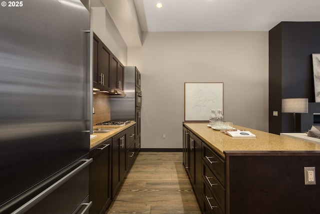 kitchen featuring built in refrigerator, a kitchen island, wood finished floors, dark brown cabinets, and backsplash