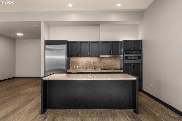 kitchen featuring sink, appliances with stainless steel finishes, decorative backsplash, a kitchen island, and hardwood / wood-style flooring