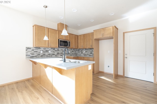 kitchen featuring light hardwood / wood-style flooring, kitchen peninsula, sink, pendant lighting, and tasteful backsplash