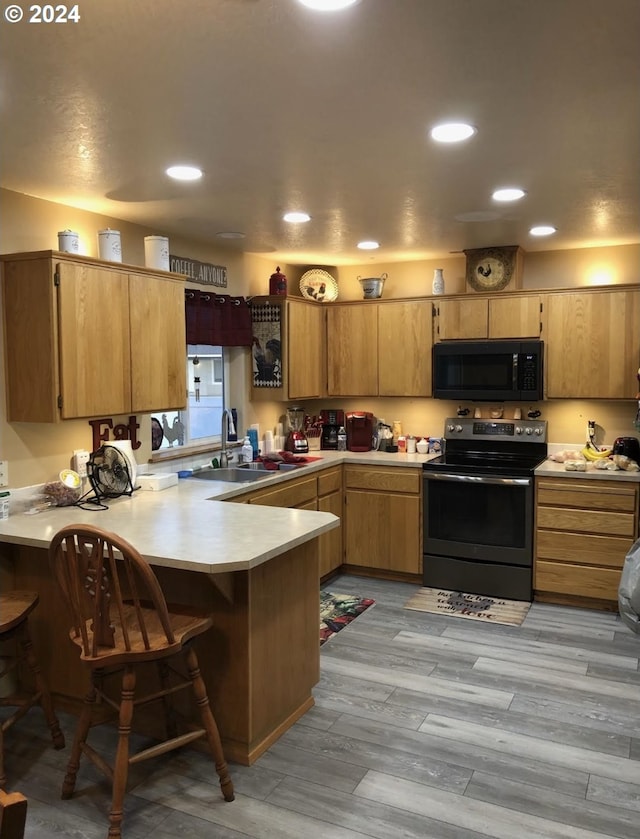 kitchen with sink, kitchen peninsula, light hardwood / wood-style flooring, electric range, and a kitchen bar