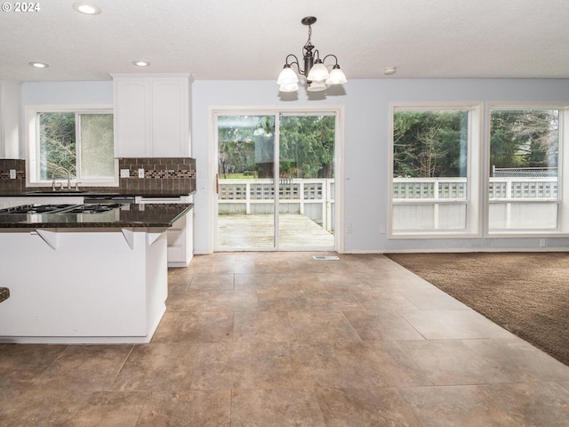 kitchen featuring dark stone counters, a breakfast bar, an inviting chandelier, white cabinets, and hanging light fixtures