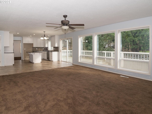 unfurnished living room featuring a textured ceiling, ceiling fan with notable chandelier, and dark carpet