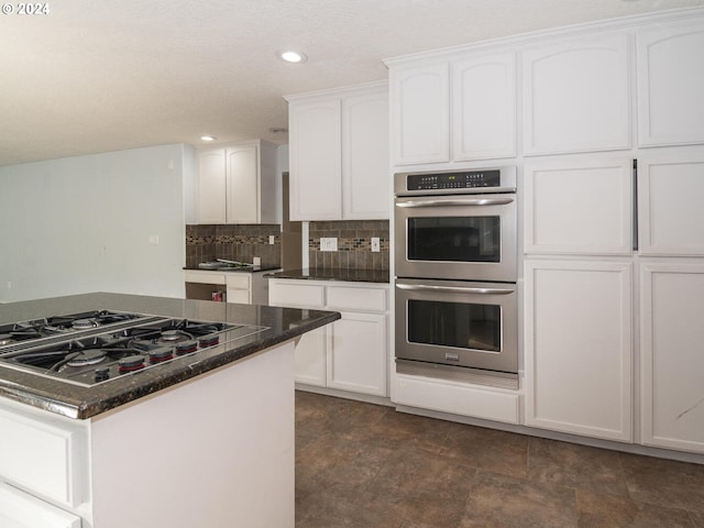 kitchen with backsplash, black gas stovetop, double oven, dark stone countertops, and white cabinetry