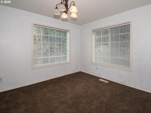 empty room with dark carpet and an inviting chandelier