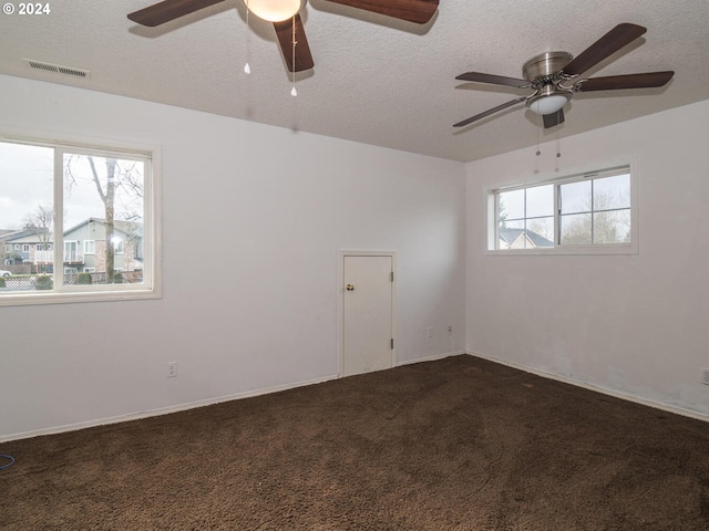 spare room with dark colored carpet, a textured ceiling, and plenty of natural light