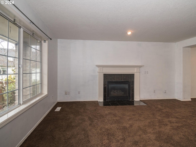 unfurnished living room featuring a tiled fireplace, a textured ceiling, and dark colored carpet